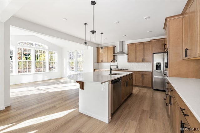 kitchen with a center island with sink, wall chimney exhaust hood, appliances with stainless steel finishes, decorative light fixtures, and light hardwood / wood-style floors