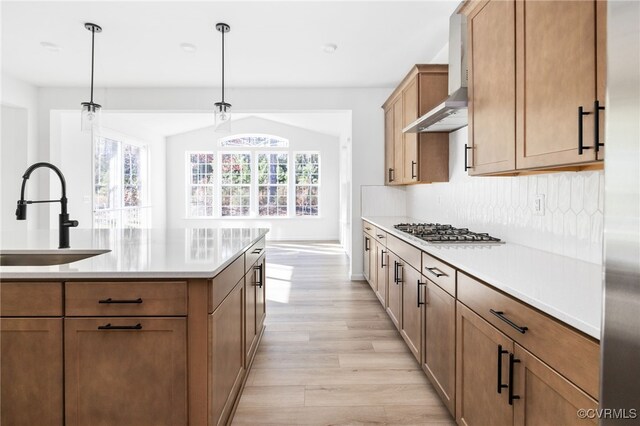 kitchen with sink, wall chimney exhaust hood, light wood-type flooring, decorative light fixtures, and stainless steel gas cooktop