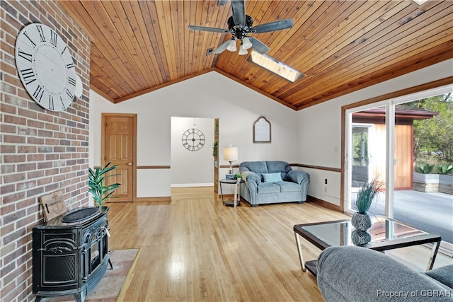 living room with wood ceiling, vaulted ceiling with skylight, ceiling fan, light hardwood / wood-style flooring, and a wood stove