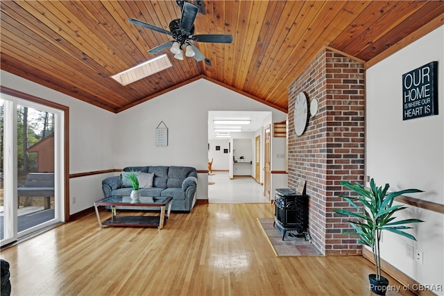 living room featuring a wood stove, vaulted ceiling with skylight, wood ceiling, and light wood-type flooring