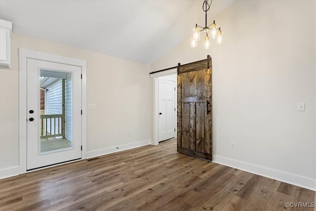 empty room featuring a barn door, wood-type flooring, and lofted ceiling