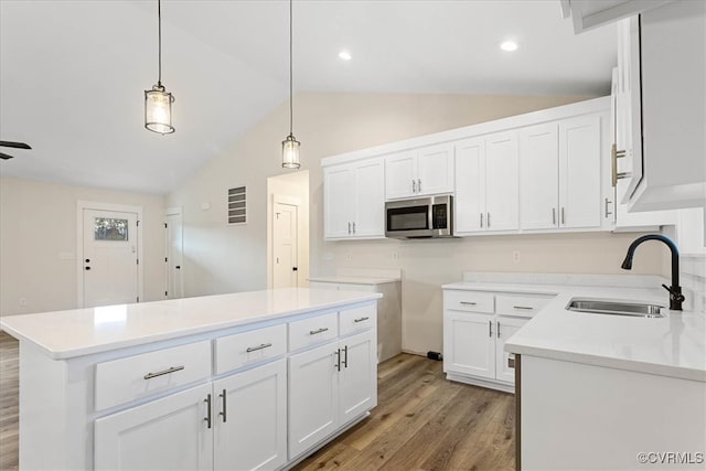 kitchen featuring white cabinets, sink, vaulted ceiling, light wood-type flooring, and a kitchen island