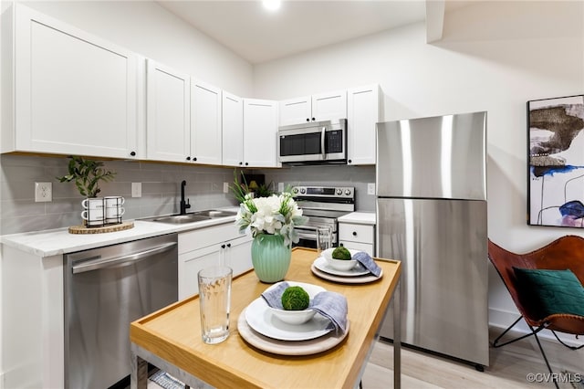 kitchen with white cabinetry, sink, tasteful backsplash, light hardwood / wood-style floors, and appliances with stainless steel finishes