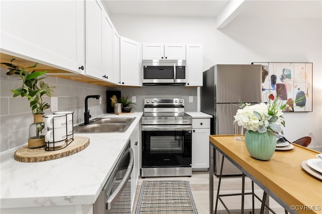 kitchen featuring white cabinetry, sink, stainless steel appliances, tasteful backsplash, and light stone counters