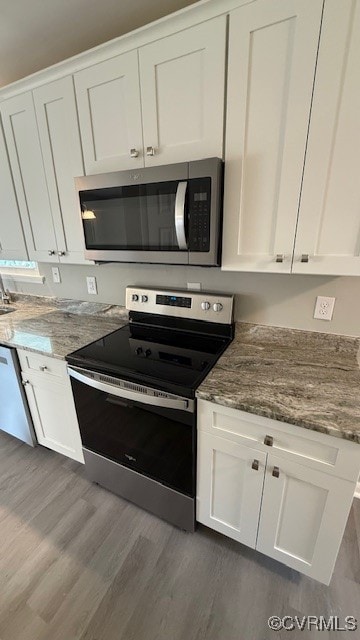 kitchen featuring white cabinets, appliances with stainless steel finishes, dark stone counters, and dark wood-type flooring