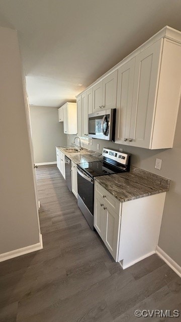 kitchen featuring white cabinets, stainless steel appliances, dark stone counters, and dark wood-type flooring