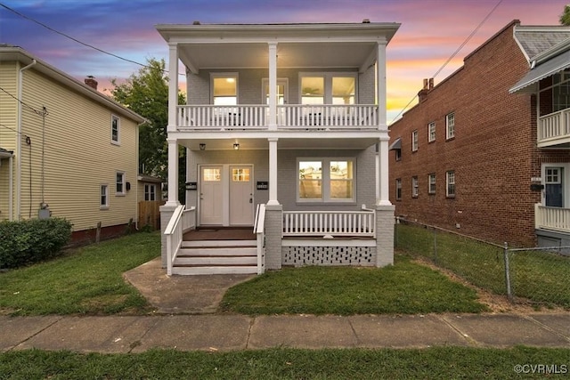 view of front facade featuring covered porch, brick siding, a front lawn, and a balcony