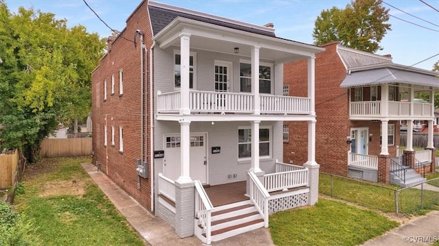 view of front facade featuring a balcony, covered porch, fence private yard, and brick siding