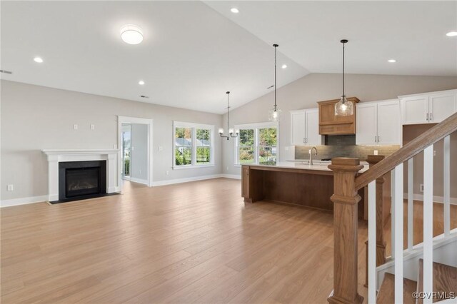 kitchen with light hardwood / wood-style flooring, a large island with sink, decorative light fixtures, lofted ceiling, and white cabinets