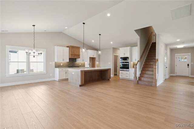 kitchen featuring light hardwood / wood-style flooring, vaulted ceiling, decorative light fixtures, a center island with sink, and white cabinets