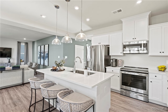 kitchen with pendant lighting, sink, stainless steel appliances, and a center island with sink