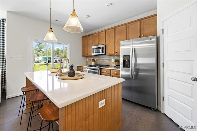 kitchen featuring decorative light fixtures, dark hardwood / wood-style flooring, stainless steel appliances, and an island with sink