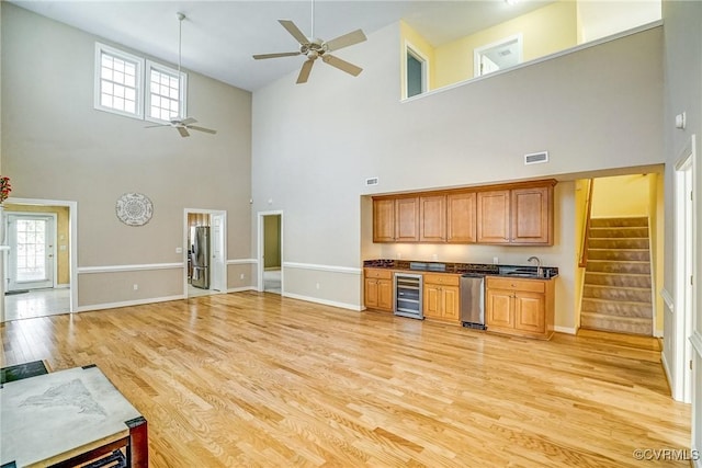 living room featuring ceiling fan, beverage cooler, light hardwood / wood-style floors, and a high ceiling