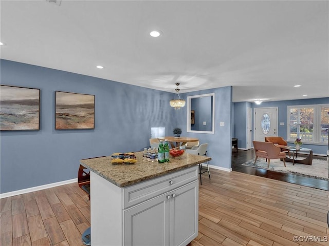 kitchen featuring a kitchen island, white cabinetry, hanging light fixtures, light stone countertops, and light wood-type flooring