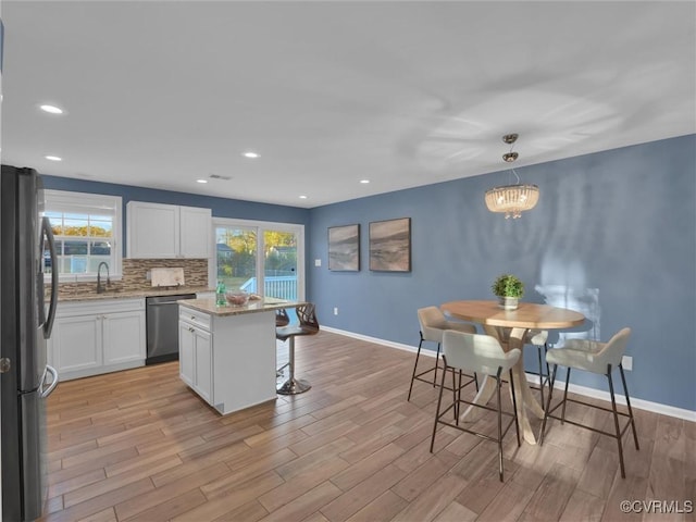 kitchen featuring a kitchen island, appliances with stainless steel finishes, pendant lighting, white cabinetry, and light hardwood / wood-style floors