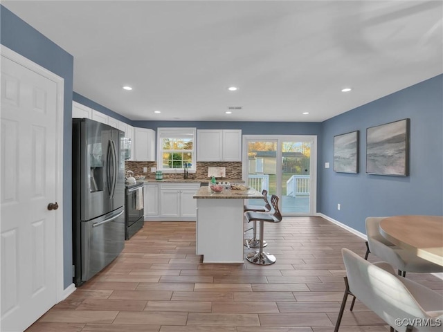 kitchen with stainless steel refrigerator with ice dispenser, a kitchen breakfast bar, a kitchen island, electric stove, and white cabinets