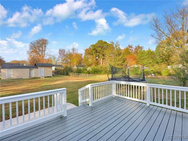 wooden terrace featuring a trampoline, a lawn, and a storage unit