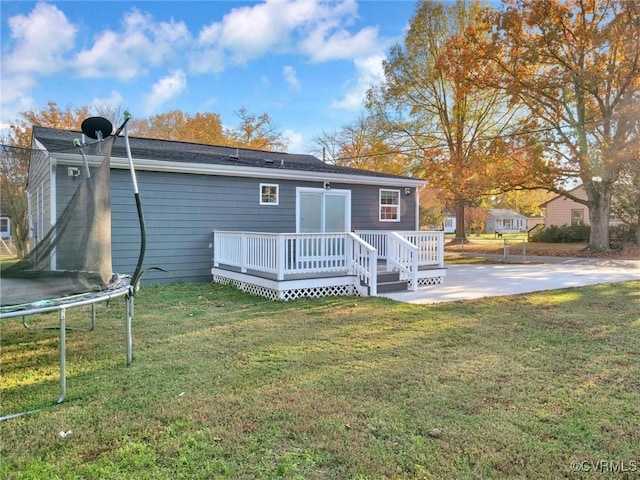 rear view of house featuring a wooden deck, a yard, a trampoline, and a patio area