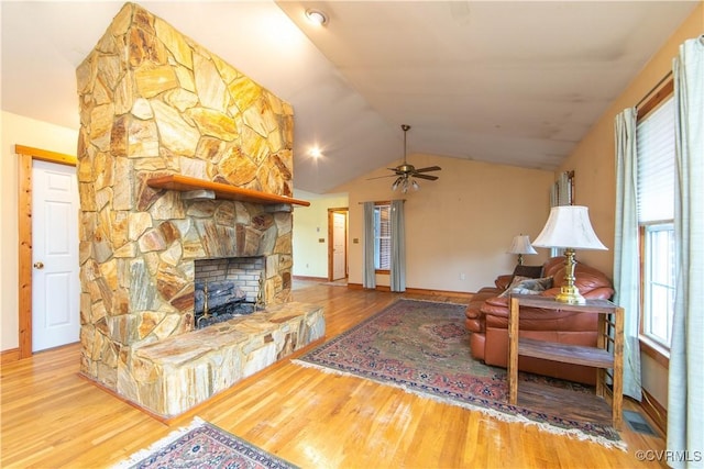 living room featuring hardwood / wood-style floors, ceiling fan, a stone fireplace, and lofted ceiling