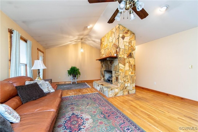 living room featuring hardwood / wood-style flooring, ceiling fan, a stone fireplace, and vaulted ceiling