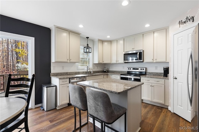 kitchen with pendant lighting, light stone counters, stainless steel appliances, and dark wood-type flooring