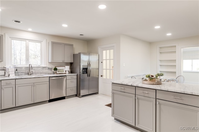 kitchen with gray cabinetry, light stone countertops, sink, light hardwood / wood-style flooring, and appliances with stainless steel finishes