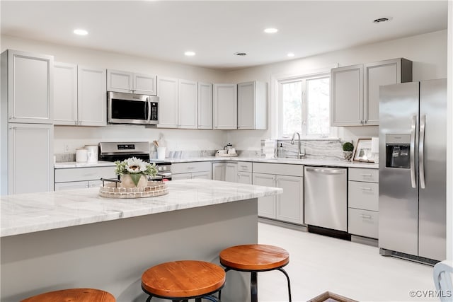 kitchen featuring sink, gray cabinets, light stone countertops, appliances with stainless steel finishes, and a kitchen bar