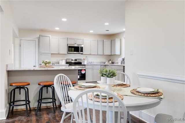 kitchen with a breakfast bar, appliances with stainless steel finishes, dark hardwood / wood-style floors, and gray cabinetry