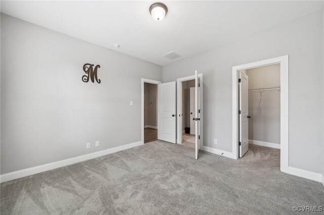 unfurnished bedroom with a spacious closet, a closet, and light colored carpet