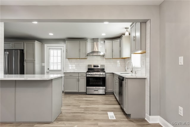 kitchen featuring gray cabinets, light hardwood / wood-style flooring, wall chimney range hood, and appliances with stainless steel finishes