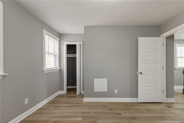 unfurnished bedroom featuring light wood-type flooring, a closet, and multiple windows