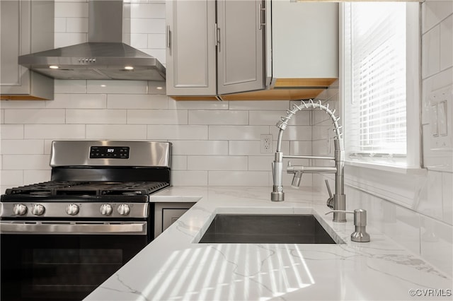 kitchen featuring gas stove, gray cabinetry, backsplash, and wall chimney range hood