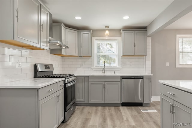 kitchen with appliances with stainless steel finishes, light wood-type flooring, gray cabinets, and sink