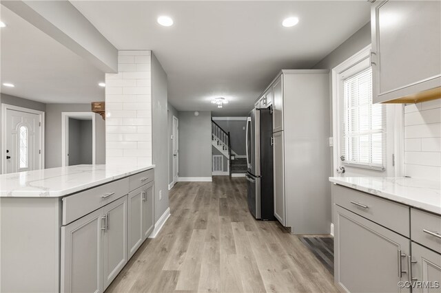 kitchen with gray cabinetry, light wood-type flooring, tasteful backsplash, light stone counters, and stainless steel refrigerator