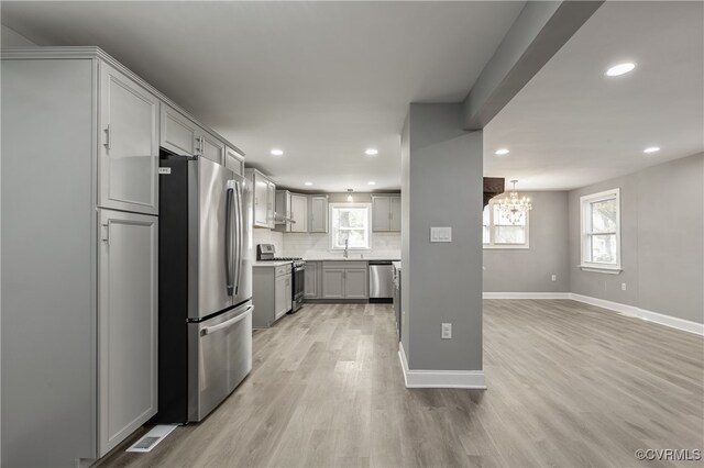 kitchen with gray cabinetry, light hardwood / wood-style flooring, tasteful backsplash, stainless steel appliances, and a chandelier