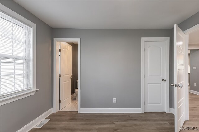 unfurnished bedroom featuring connected bathroom and hardwood / wood-style flooring