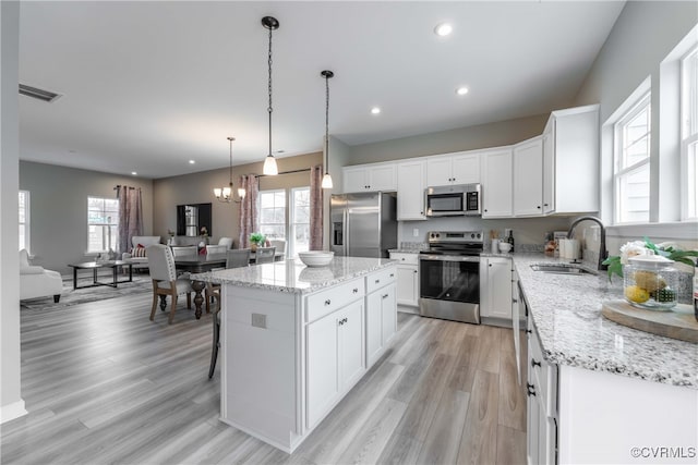 kitchen with pendant lighting, a kitchen island, white cabinetry, stainless steel appliances, and sink