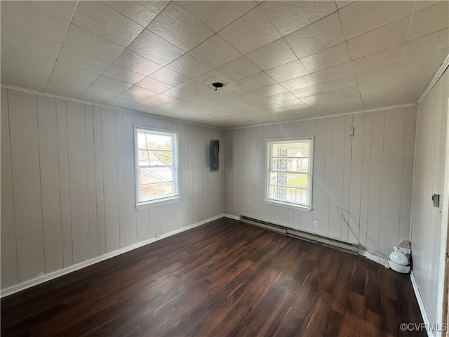 empty room with a baseboard heating unit, wooden walls, and dark wood-type flooring