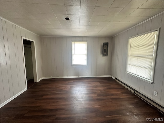 spare room featuring dark hardwood / wood-style floors, wood walls, ornamental molding, and a baseboard heating unit