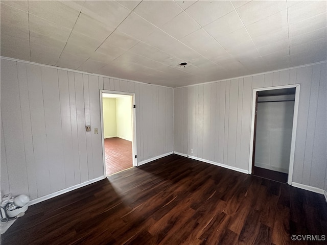 unfurnished bedroom with wood walls, a closet, and dark hardwood / wood-style floors