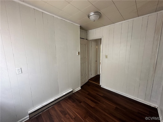 empty room featuring dark hardwood / wood-style flooring, baseboard heating, and wooden walls