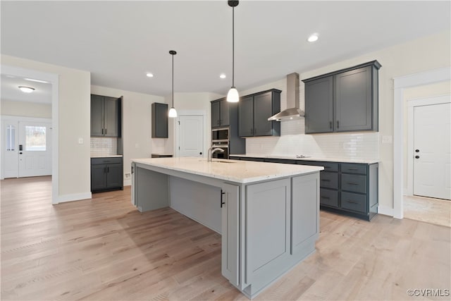 kitchen featuring light hardwood / wood-style floors, a center island with sink, and wall chimney exhaust hood