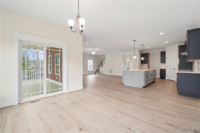 kitchen with pendant lighting, plenty of natural light, light hardwood / wood-style floors, and an island with sink