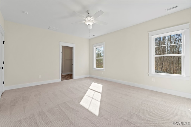 unfurnished bedroom with a walk in closet, light colored carpet, a closet, and ceiling fan