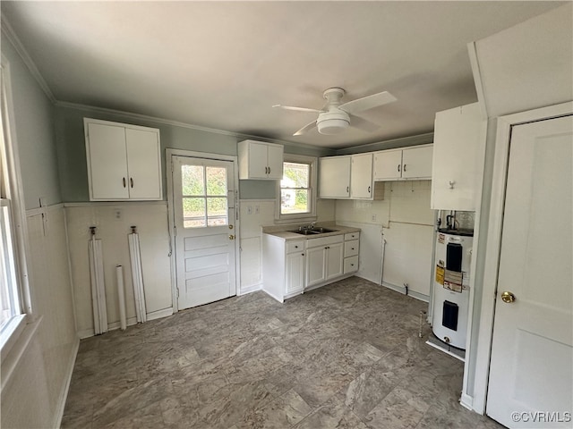 kitchen with electric water heater, ceiling fan, crown molding, sink, and white cabinets