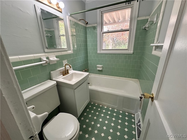 full bathroom featuring tiled shower / bath combo, toilet, tile walls, and vanity