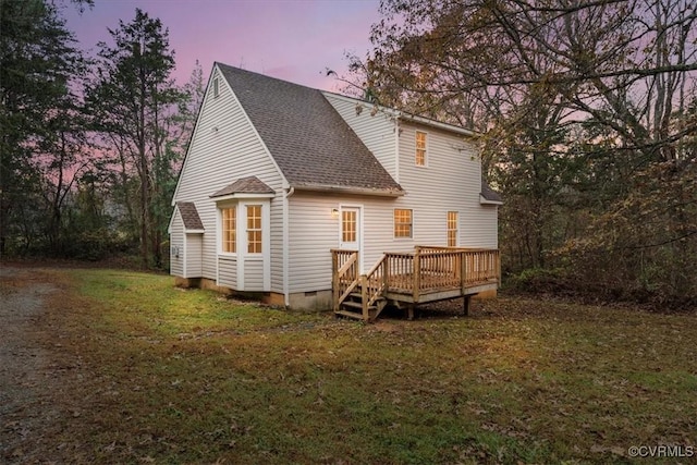 back house at dusk with a yard and a deck