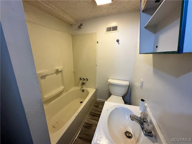 full bathroom with sink, bathing tub / shower combination, hardwood / wood-style floors, a textured ceiling, and toilet