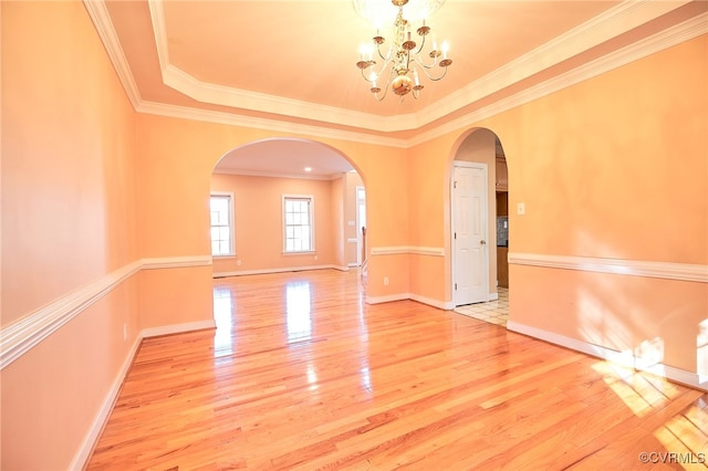 spare room featuring wood-type flooring, crown molding, a tray ceiling, and a chandelier