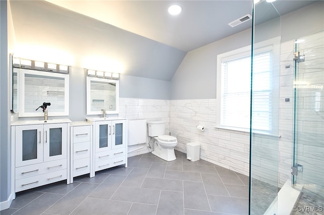 bathroom featuring tile patterned flooring, vaulted ceiling, toilet, vanity, and tile walls